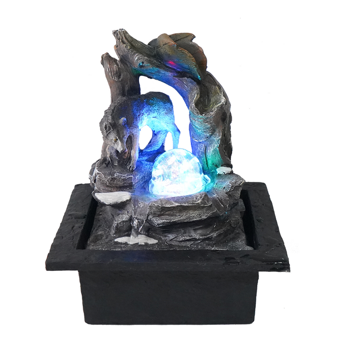 A fountain featuring a realistic wolf design with water flowing over it, surrounded by rocks, within a black pot.