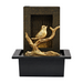 A gold-colored bird fountain with a bird design perched on a branch, set in a black square-shaped base.