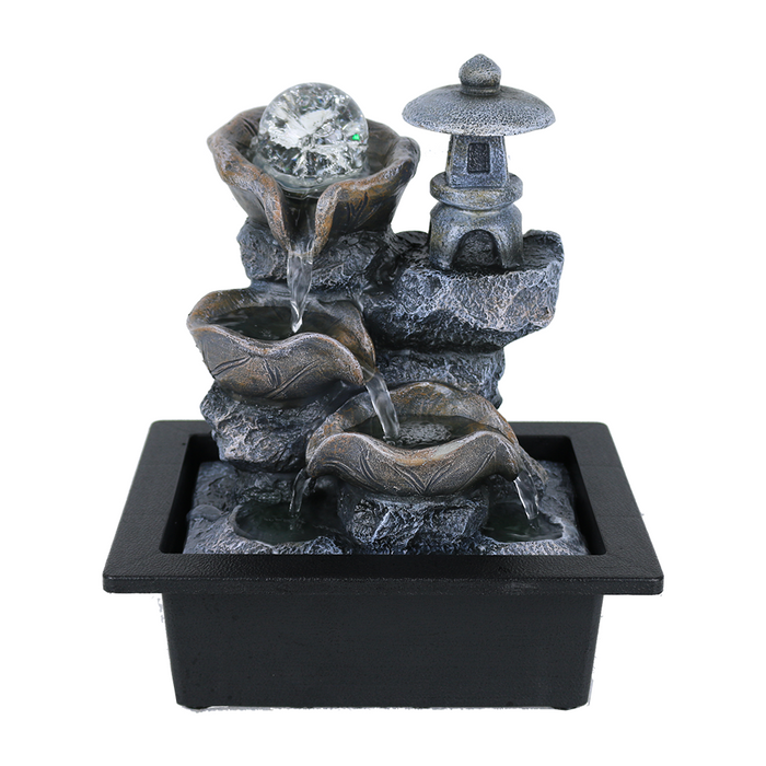 A Zen-inspired water feature with a minimalist design, consisting of a central sphere and a tiered structure with water flowing downwards into a black basin, surrounded by a circular platform.