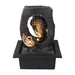 A Zen-inspired water feature fountain with a bronze-colored meditating Buddha figure on a black base, with water flowing over the Buddha's hand.