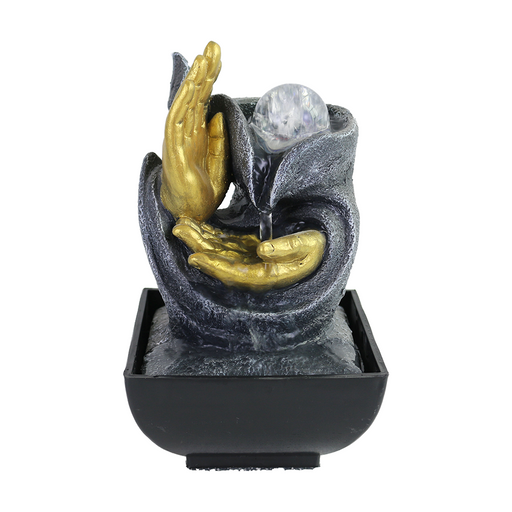 A Zen-inspired water feature with a pair of gold-colored hands holding a water sphere, set in a black base.