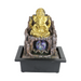 A gold-colored statue of Ganesha, the Hindu god of wisdom and prosperity, seated on a base resembling a tree with a water feature in the center.